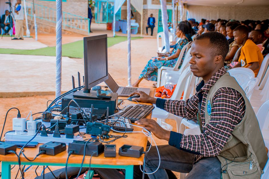 Technician managing electrical and computer setup at an outdoor event with attentive audience.