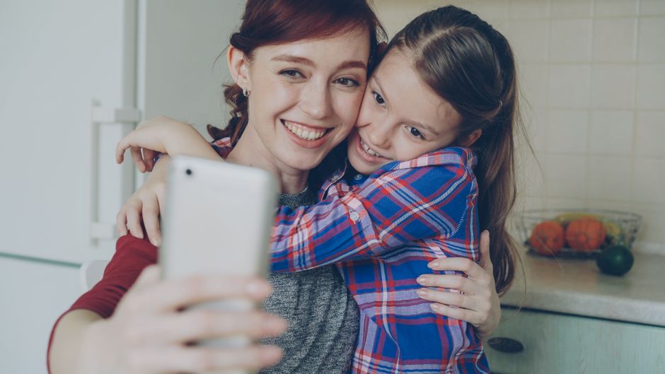 Smiling mother and daughter taking a selfie in a cozy indoor setting.