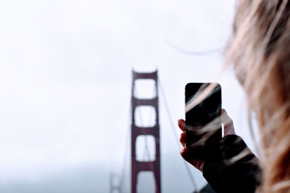 A woman takes a photo of the foggy Golden Gate Bridge, highlighting modern travel and technology.