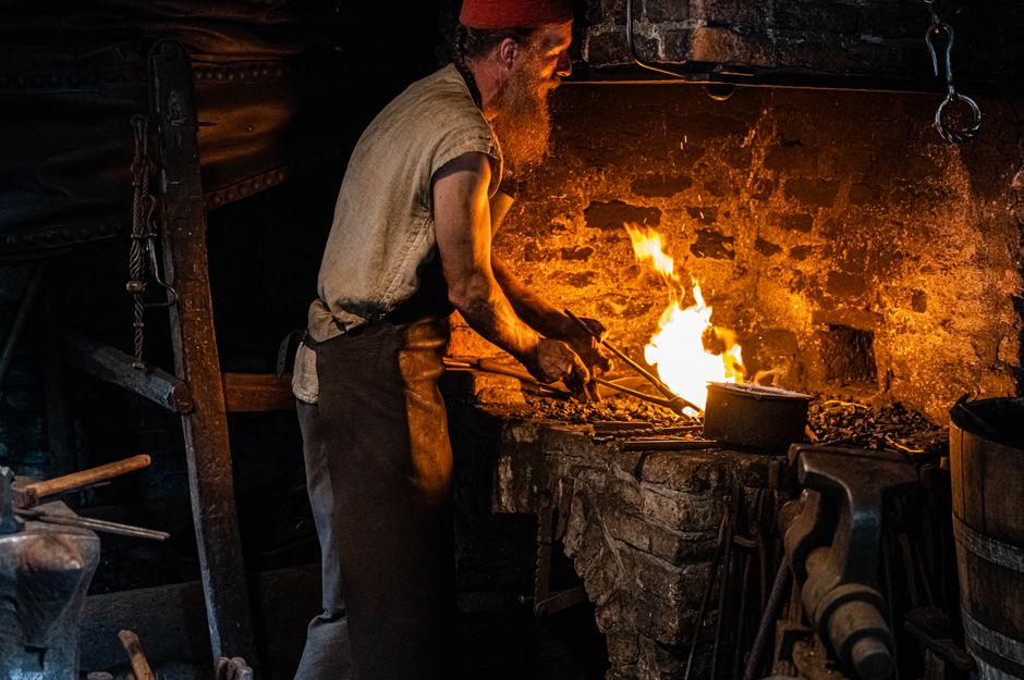 A skilled blacksmith shapes metal in a dimly lit forge, highlighting craftsmanship and tradition.