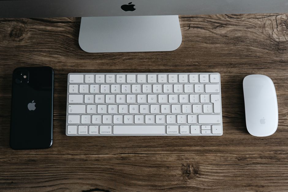 A minimalist workspace featuring a smartphone, keyboard, and mouse on a wooden desk.