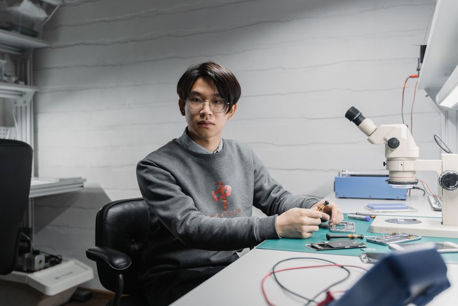 Asian man working with soldering tools and microscope on electronics in a lab setting.