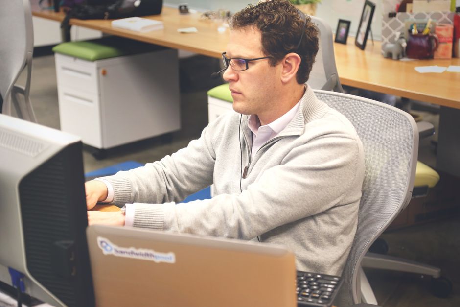 Focused man working at a computer in a modern office cubicle, wearing glasses and headphones.