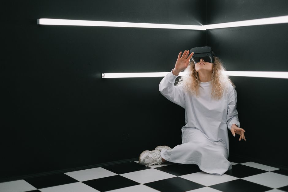A woman in a white dress explores virtual reality in a modern, dark room.