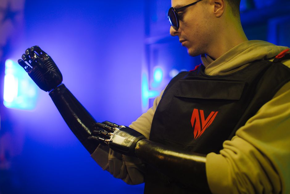 A man examines his advanced prosthetic arm in a neon-lit futuristic setting.