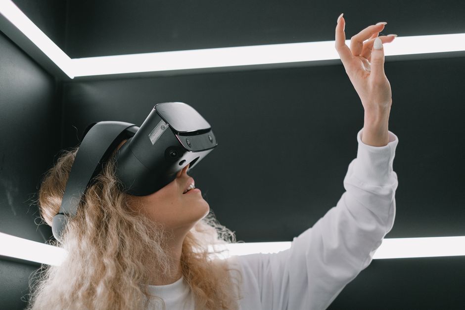 A woman wearing a headset engages with virtual reality, reaching out her hand.
